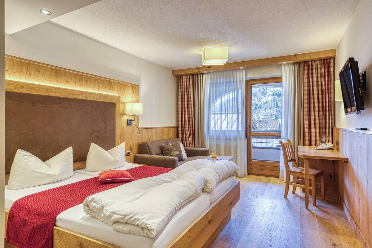 A hotel room with a large bed, a desk, a chair, a television, and a window with curtains.