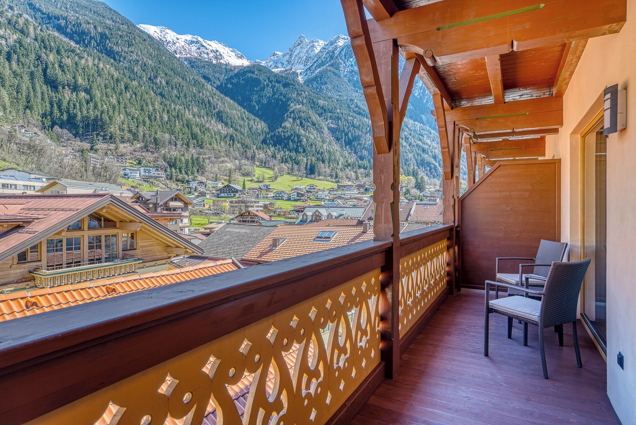 A balcony with a view of a mountain village and snow-capped peaks.