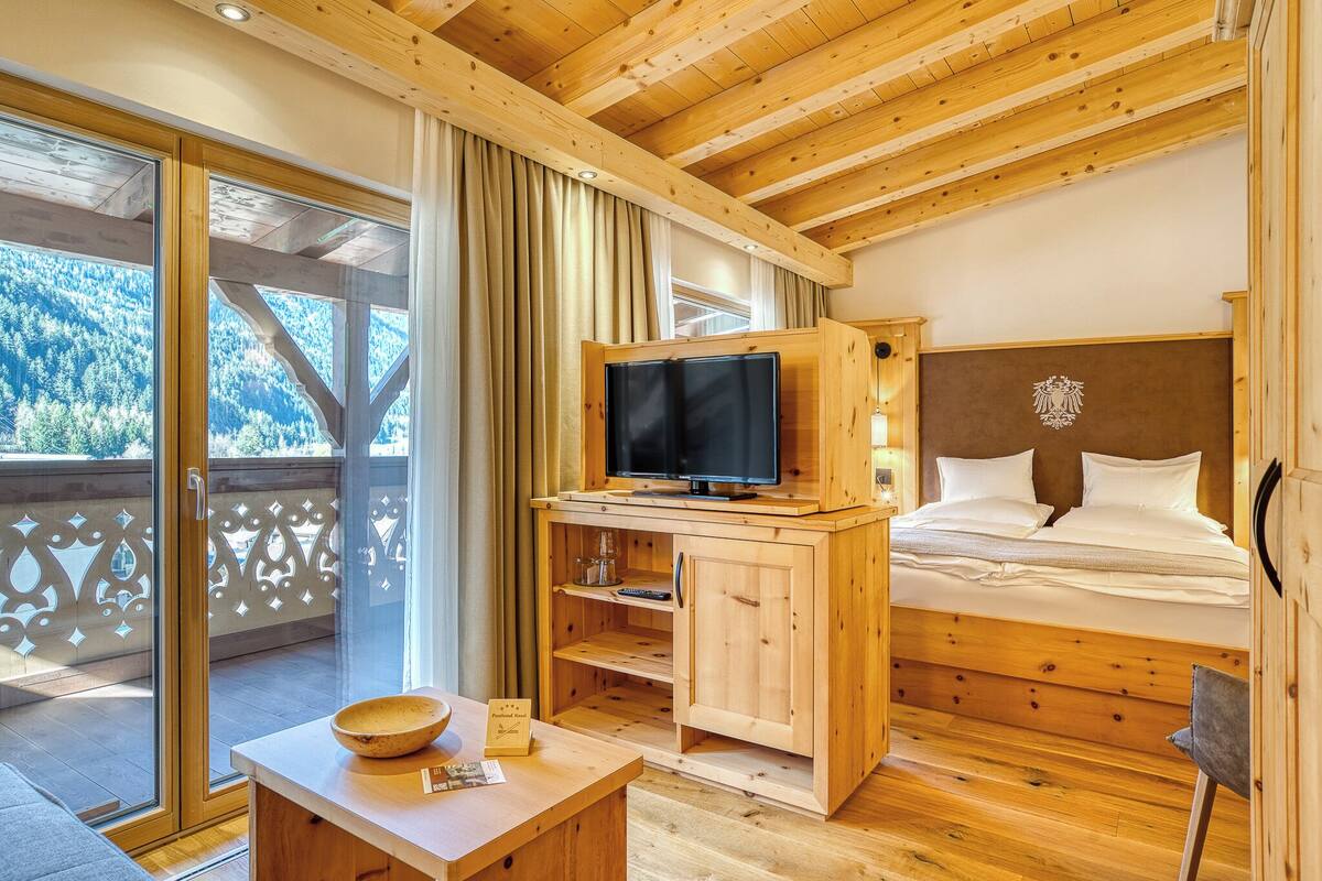 A wooden bedroom with a bed, TV, and a balcony with a view of the forest.