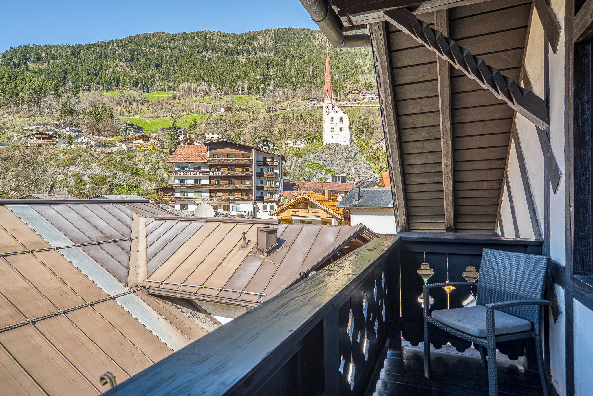 A balcony with a chair, a view of buildings, and a church in the background.