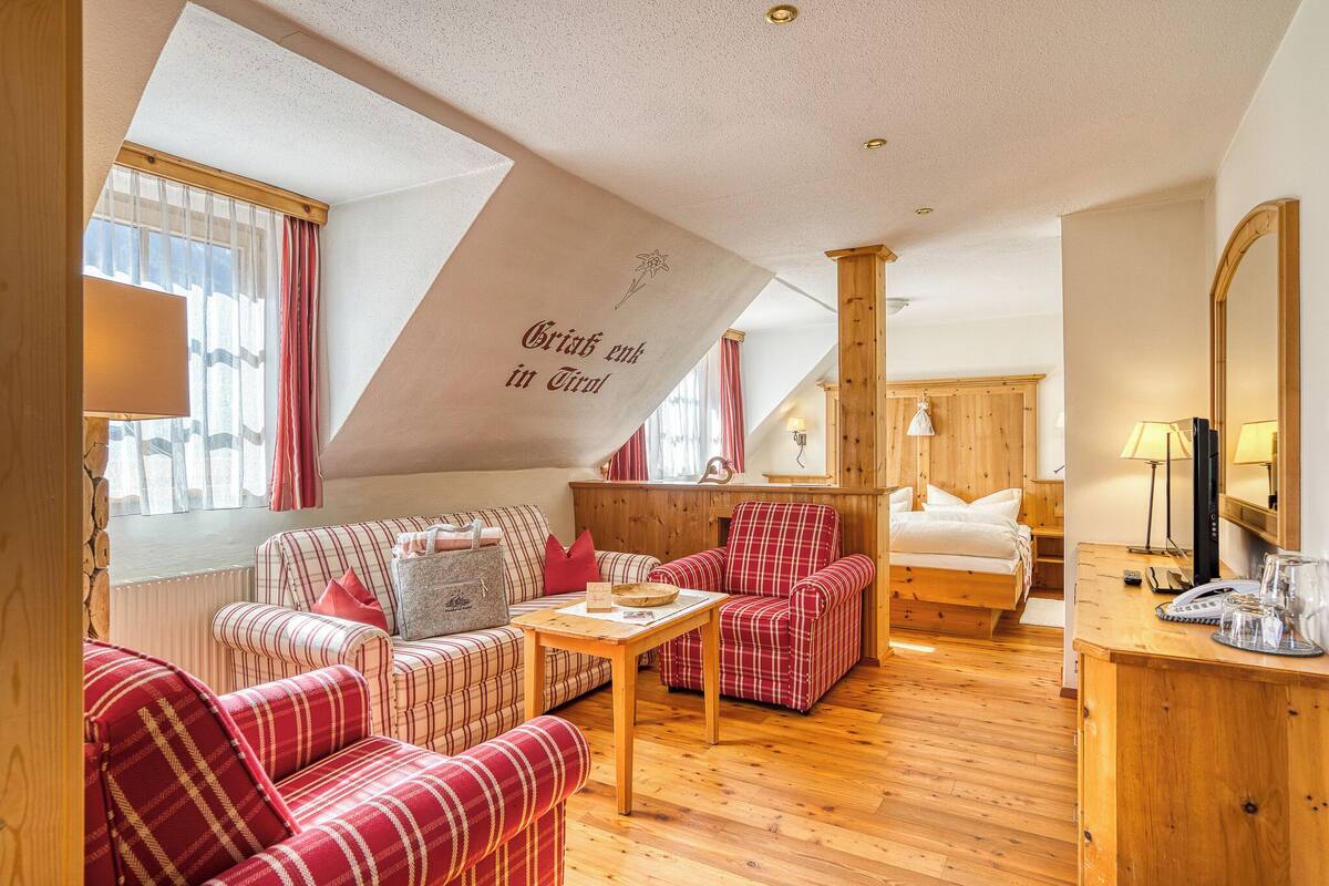 A cozy room with a bed, a sofa, a chair, a small table, and a wooden dresser.