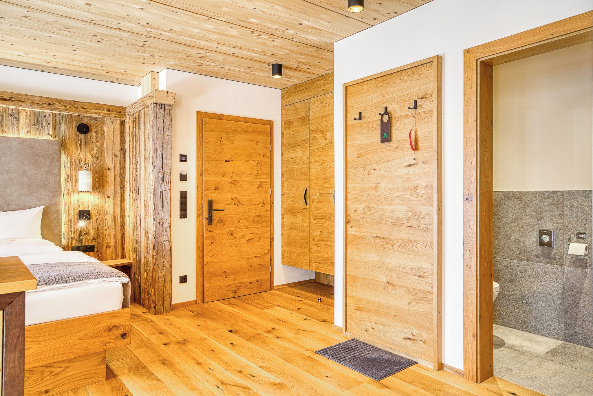 A wooden-floored room with a bed, a wardrobe, and a shower area.