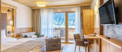 Habitación de hotel con techo de madera, cama con banco, escritorio con silla, televisor y vistas a un bosque nevado.