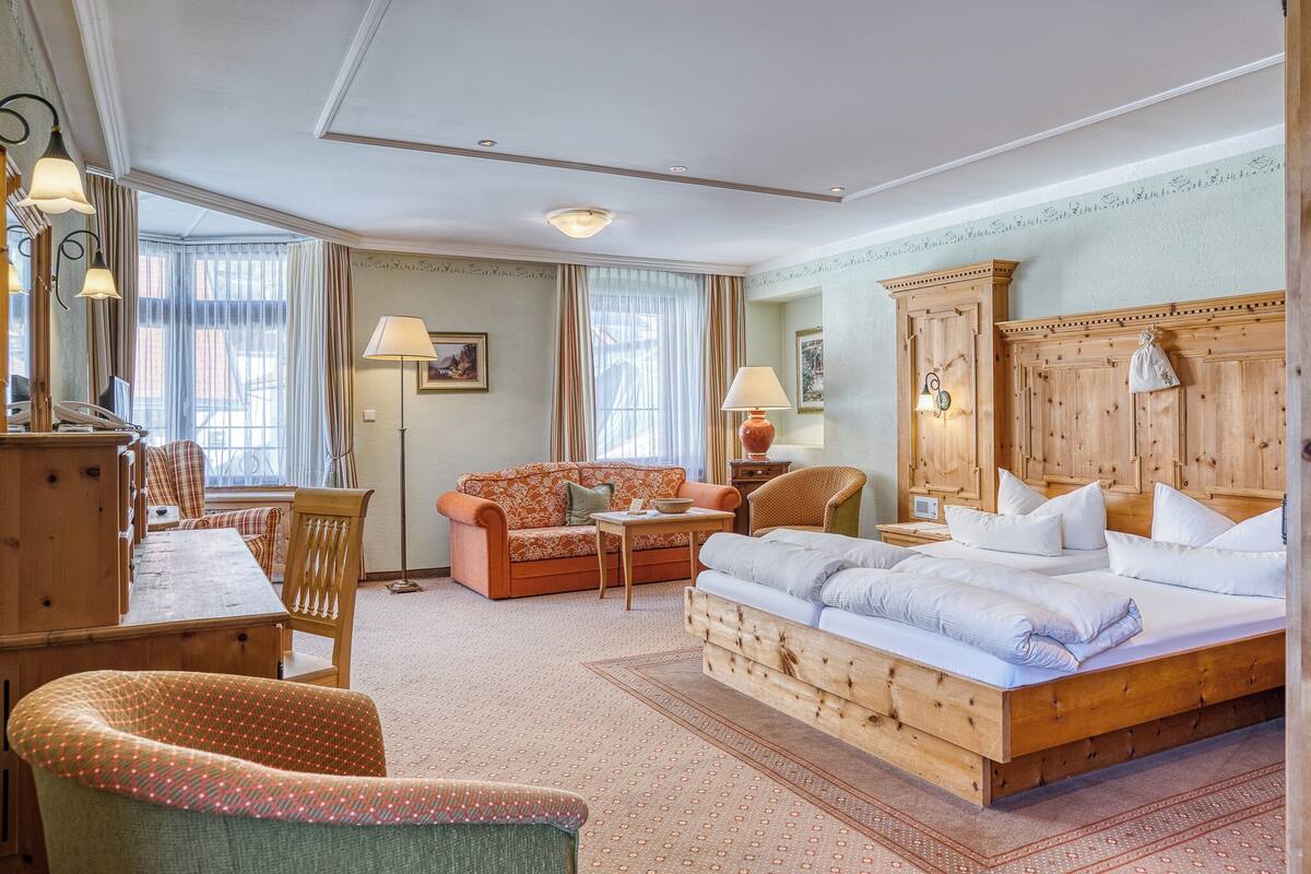 A hotel room with a wooden bed, a sofa, a dining table, and a chair.