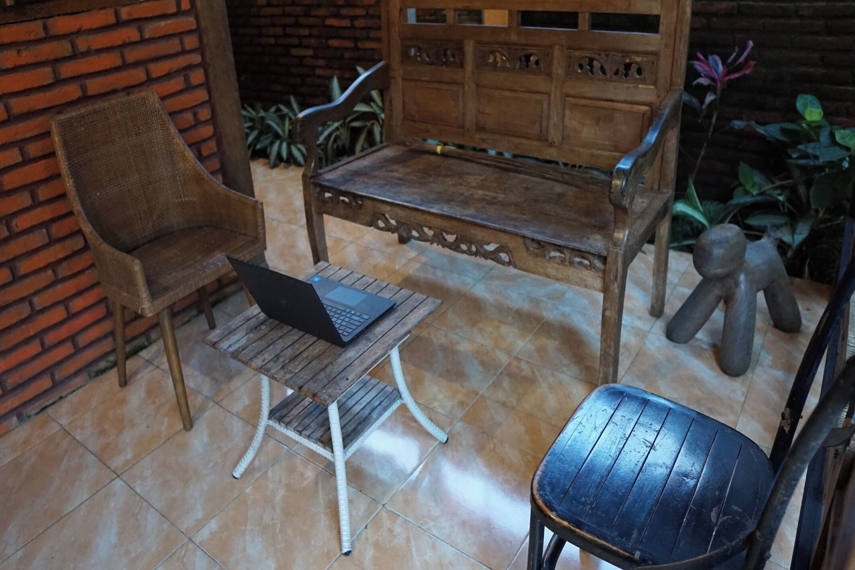A wooden bench with a laptop on a small table, a wicker chair, and a statue.