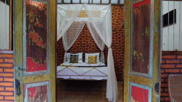Una habitación con una cama, mosquitera y pared de ladrillo.