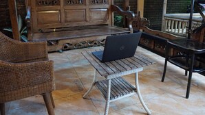 Un banco de madera con una laptop sobre una pequeña mesa, sillas de mimbre y un muro de ladrillo al fondo.
