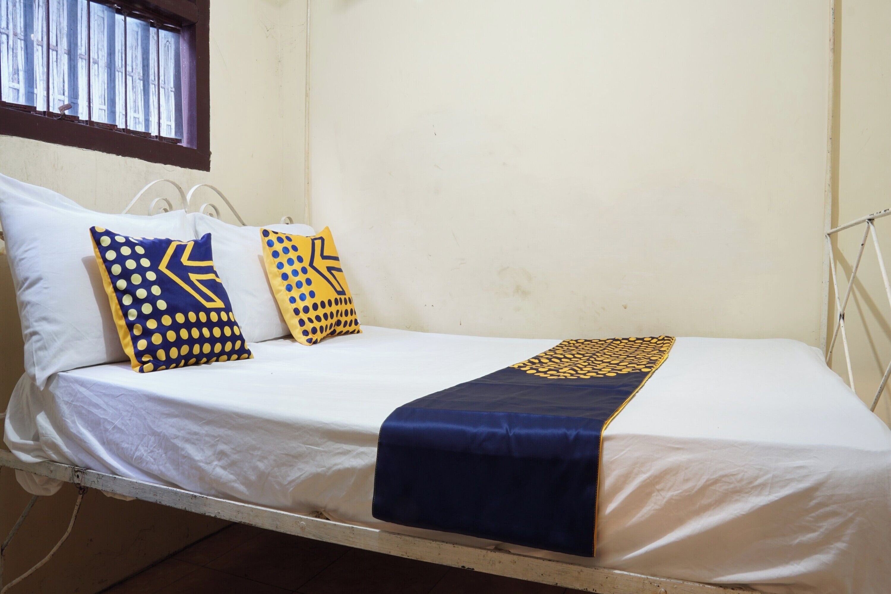 Un letto singolo con lenzuola bianche, due cuscini a motivi geometrici e una coperta blu.