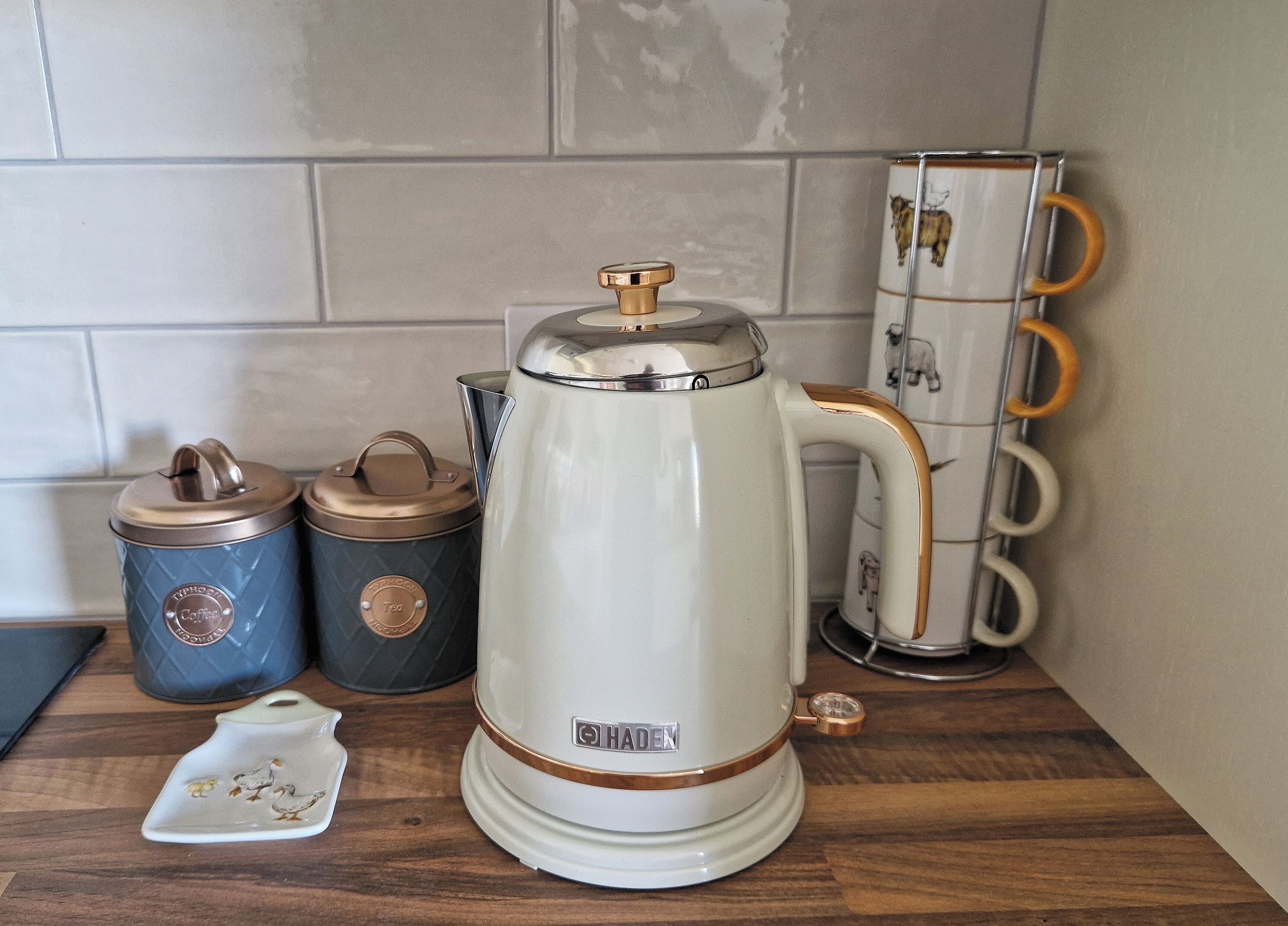 A coffee maker with a lid, two containers with lids, and a small ceramic plate with a design.