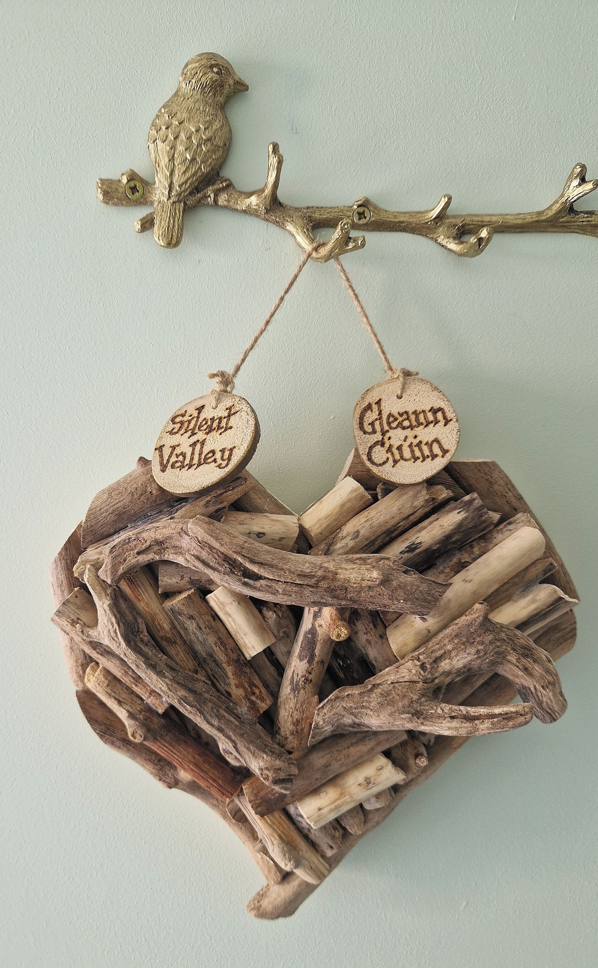 A rustic wooden nest with two wooden tags hanging from a branch, and a small owl figurine above.