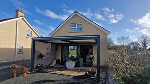 A house with a covered patio area, a fire pit, outdoor furniture, and a dog. - Gleann Ciuin (Newry)