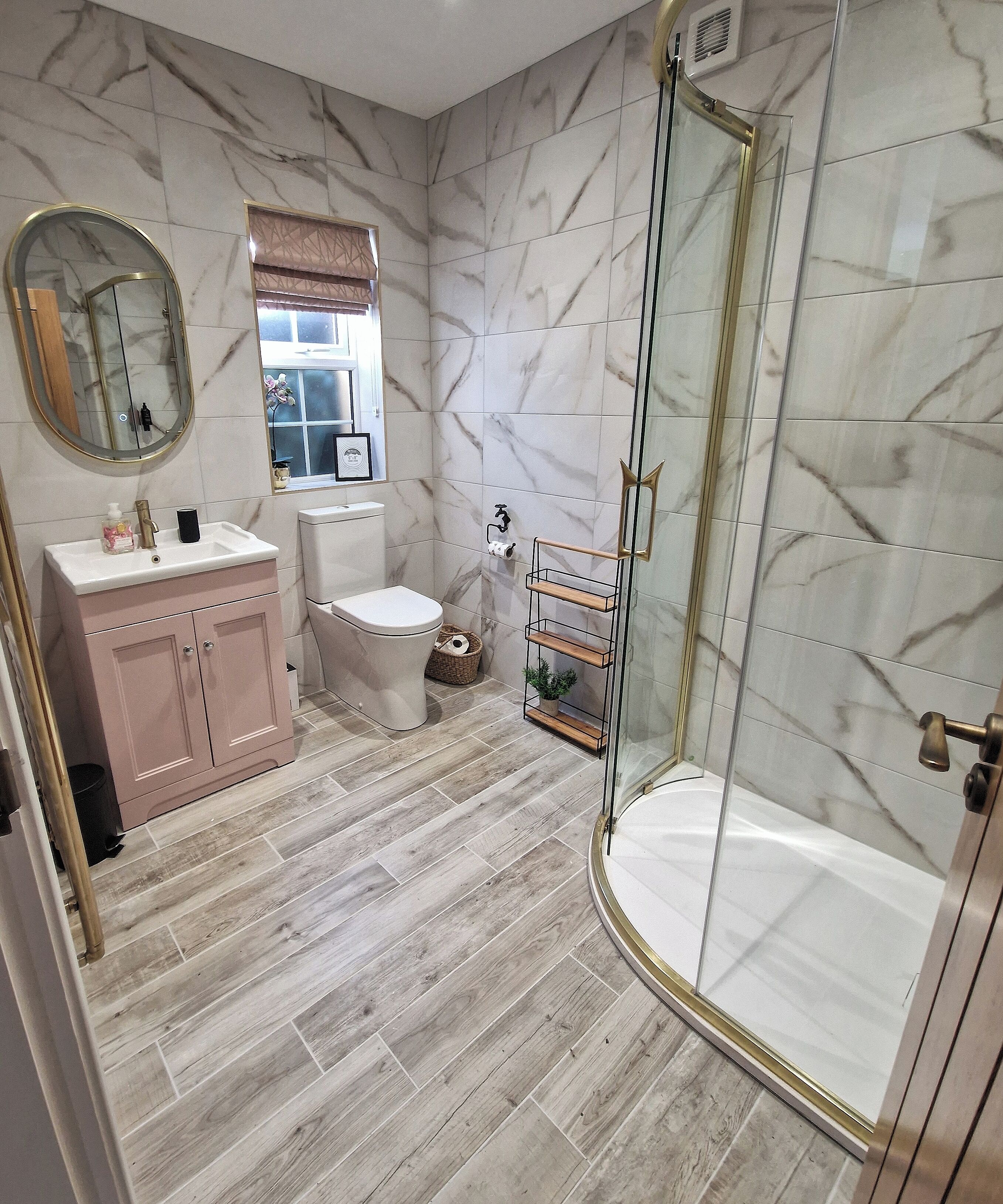 A bathroom with a marble wall, a toilet, a sink with a mirror, and a glass-enclosed shower.