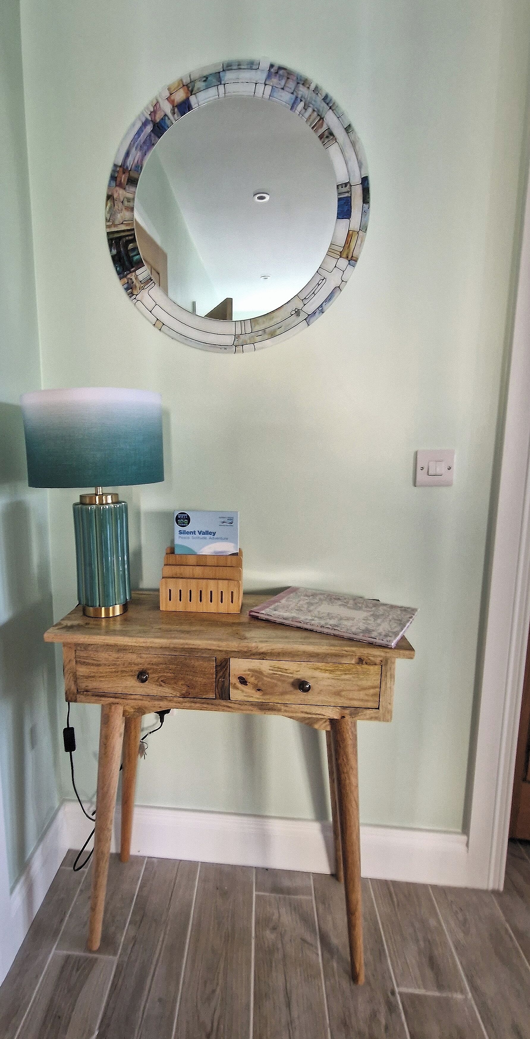 A wooden desk with a lamp, a mirror, and a box of tissues.