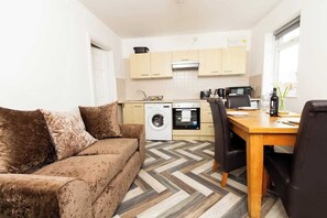 A compact living space with a sofa, a dining table, a washing machine, and a kitchen area. - Cosy & Compact Apartment in Swinton (Manchester)