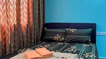 Una cama bien hecha con una colcha de estampado de hojas, dos almohadas y toallas dobladas.