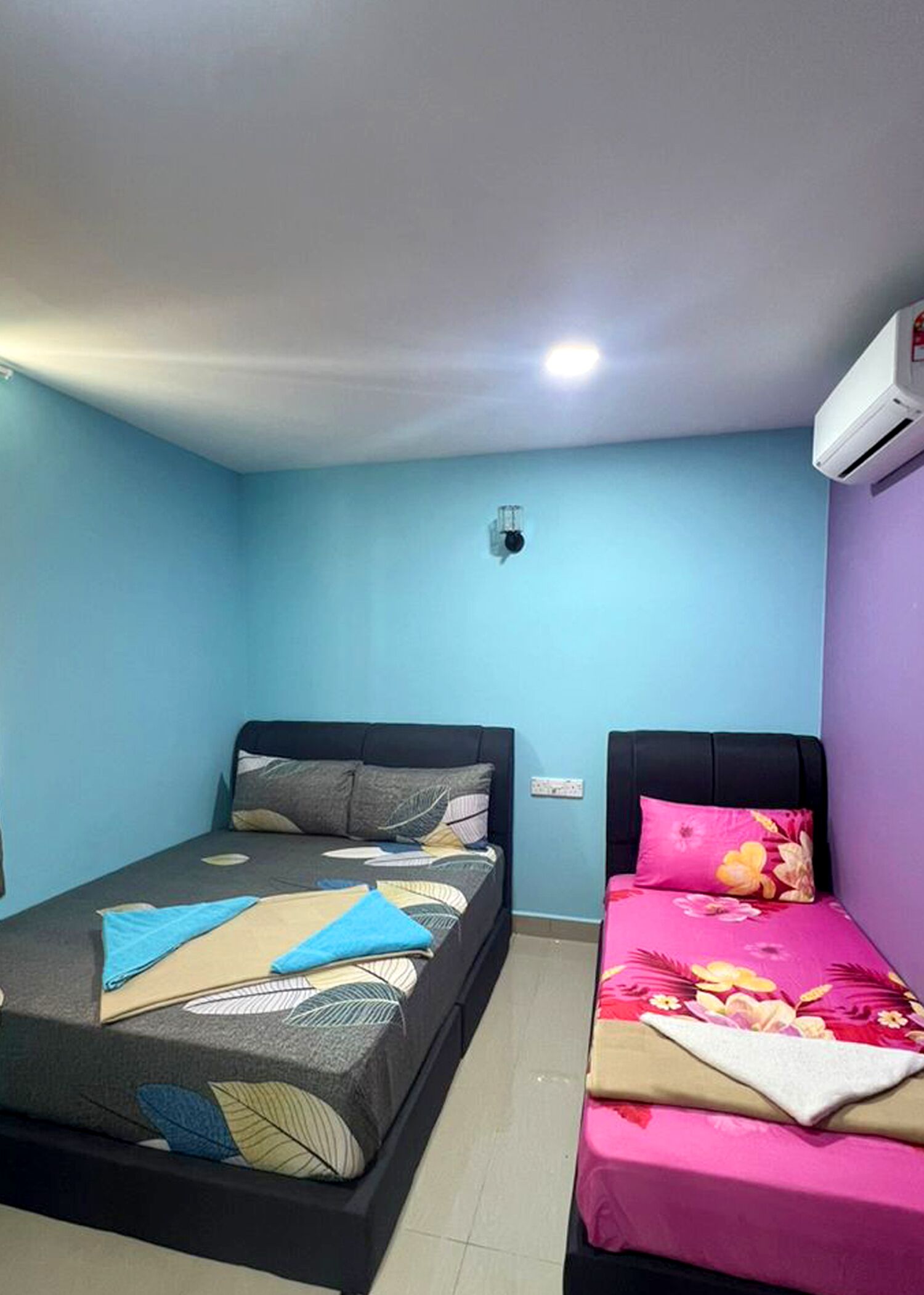 A room with two beds, one with a patterned bedspread and the other with a floral bedspread.