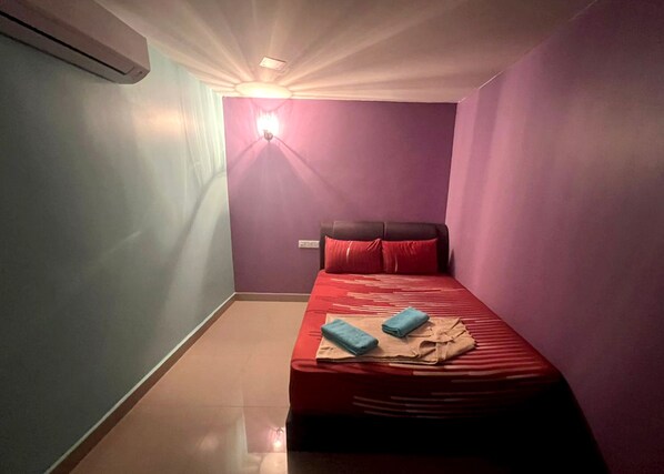 Una habitación pequeña y funcional con una cama individual, una lámpara en la pared y un equipo de aire acondicionado.