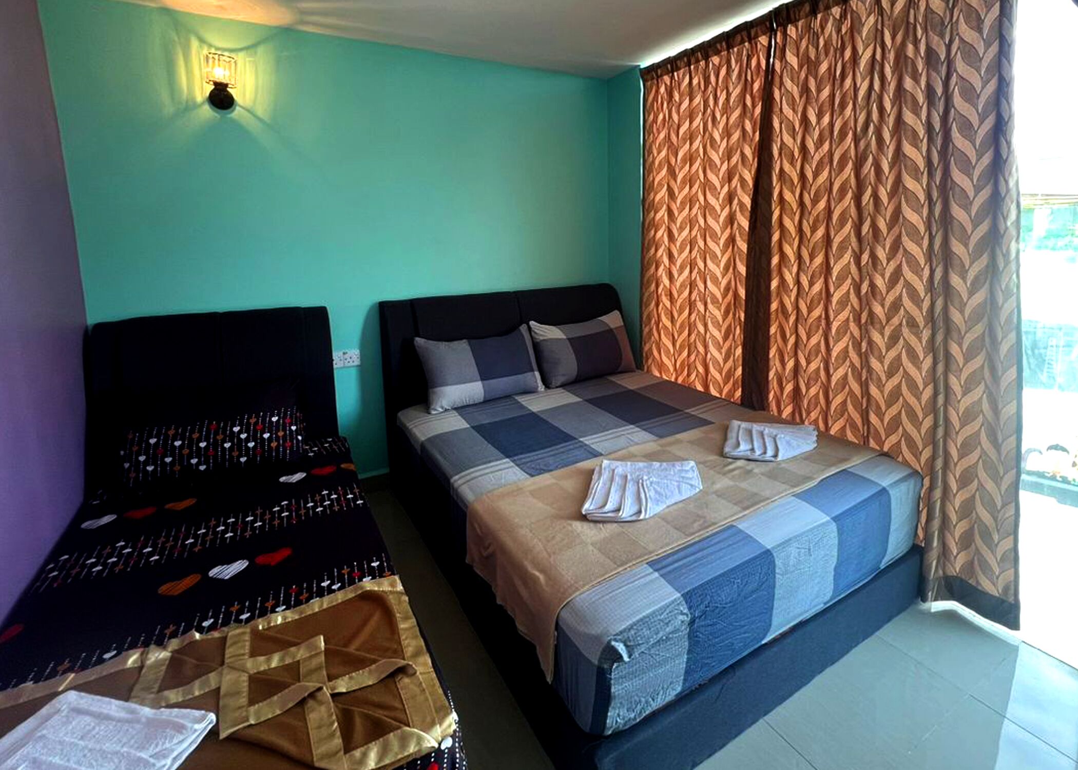 A hotel room with a bed, a small table with a decorative cloth, and a wall-mounted light fixture.