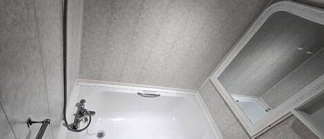 A bathroom with a white bathtub, a handheld showerhead, and a mirror.