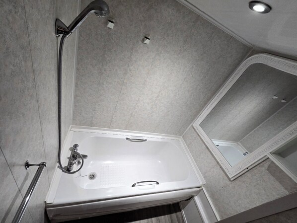A bathroom with a white bathtub, a handheld showerhead, and a mirror. - Wilsons Lodge (Blackpool)