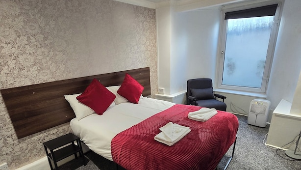 Quarto de hotel com cama, cadeira, janela e parede com padrão floral.
