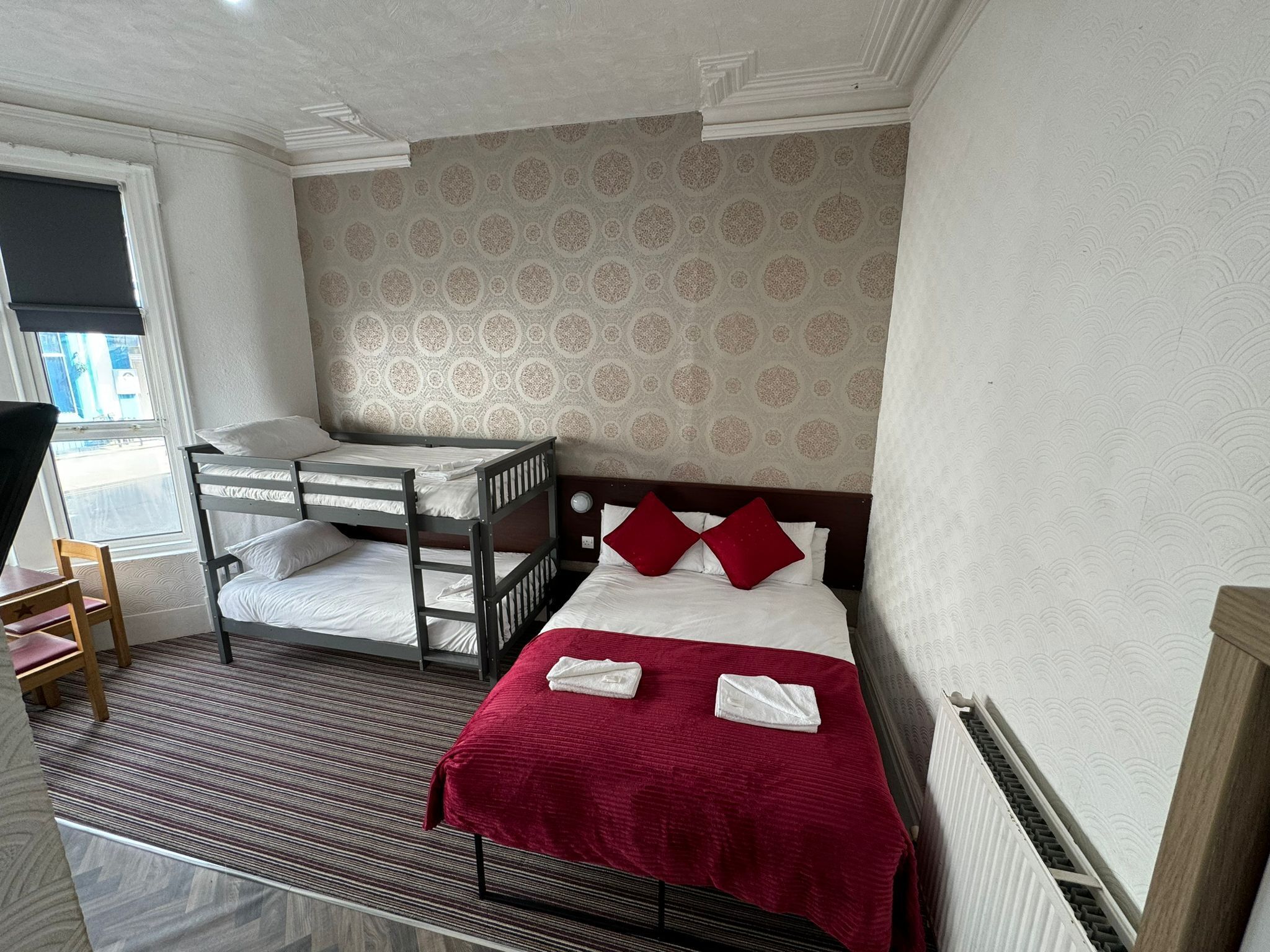 Una habitación de hotel con literas, una manta roja y un papel tapiz estampado.