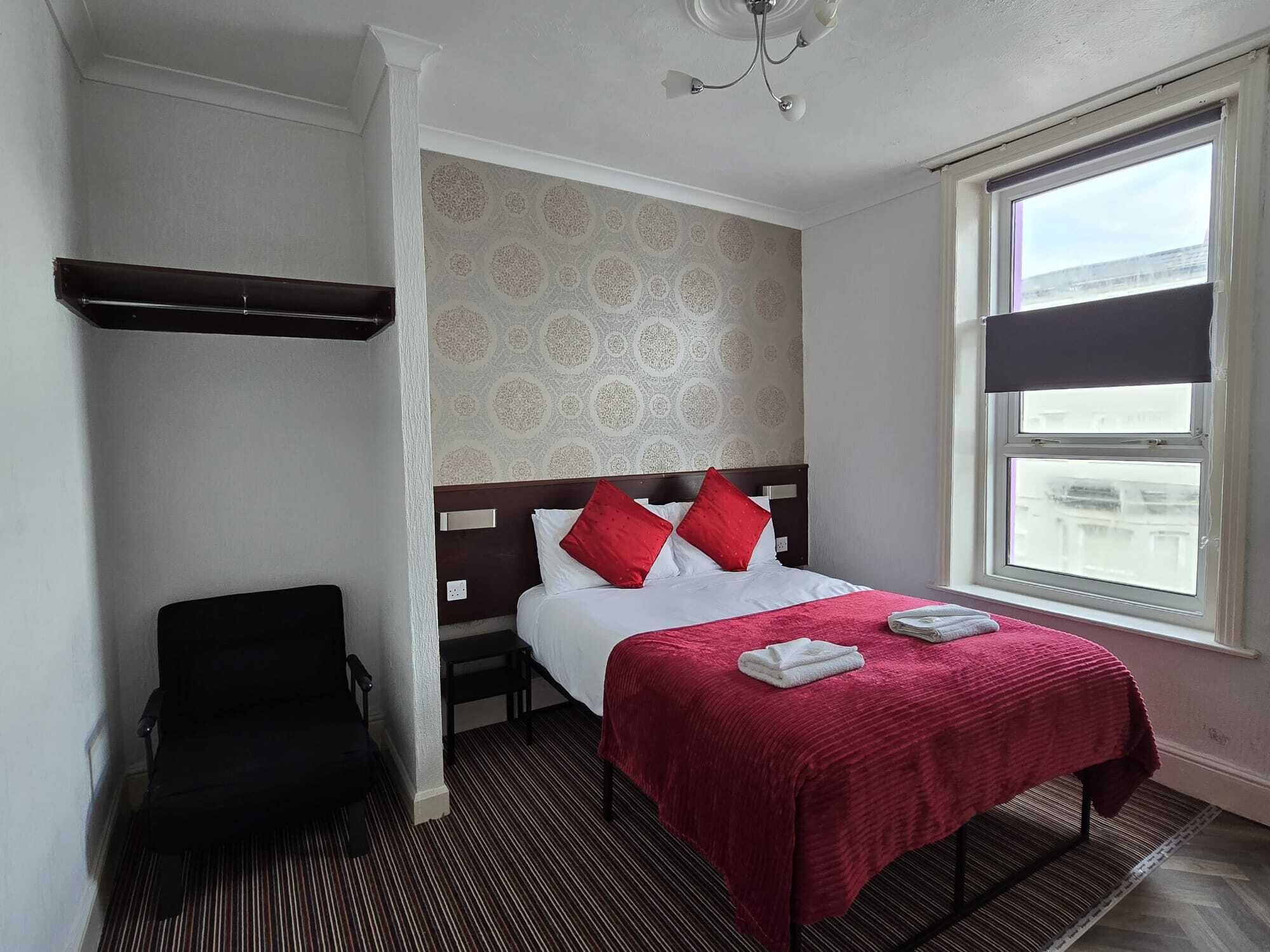 A hotel room with a bed, a chair, a window, and a patterned wall.