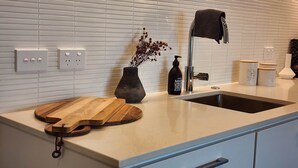 A kitchen with a white countertop, a sink, a vase with dried flowers, a cutting board, and a bottle of black soap. - Enfield Lux- Brand New Apartment (Auckland)