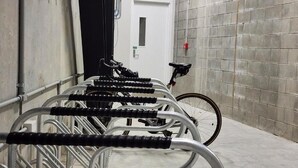 A row of bicycles parked in a covered area with a tiled wall and a door in the background. - Enfield Lux- Brand New Apartment (Auckland)