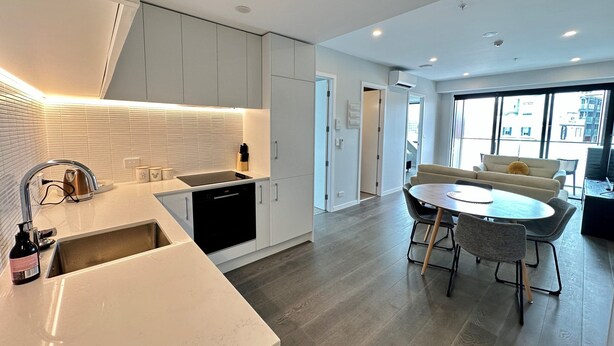 A modern kitchen with a built-in oven, a sink, and a dining area with a round table and chairs. - Enfield Lux- Brand New Apartment (Auckland)