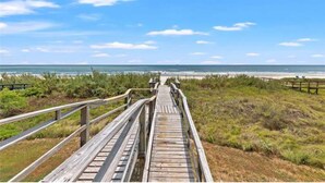 A wooden boardwalk leading to a beach with a clear sky.