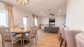 A spacious dining area with a wooden table and chairs, a grey sofa, and a television in the background.