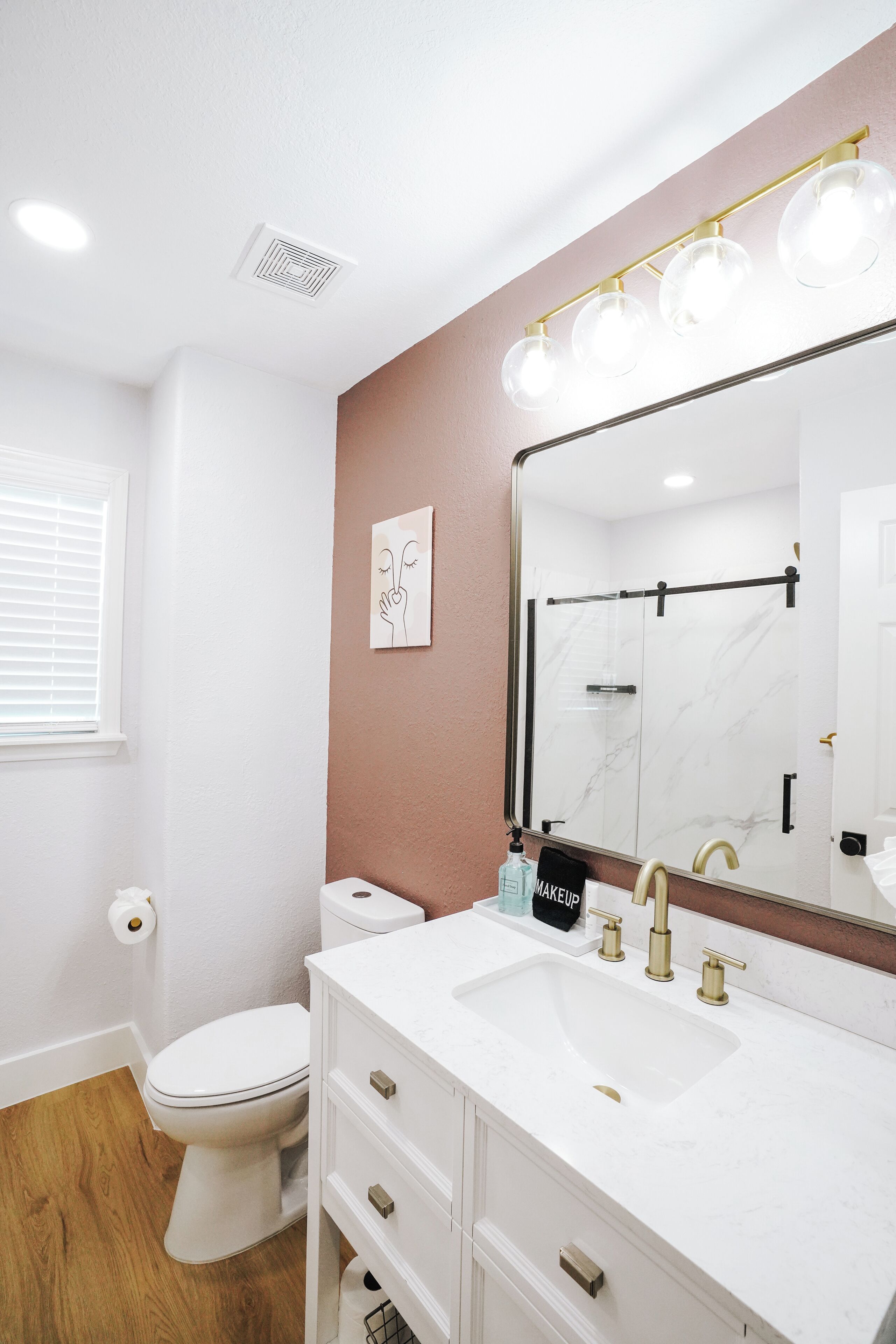 A bathroom with a white toilet, a sink with gold fixtures, and a mirror with lights.