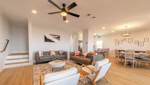 A spacious living area with a ceiling fan, a dining table with chairs, and a staircase leading to an upper level.