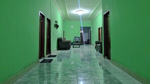 Un pasillo con paredes verdes y piso de baldosas que conduce a una sala de estar con televisor y sofá.