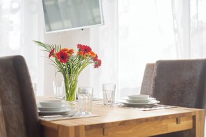 A dining table set with plates, glasses, and a vase with flowers. - Alpen-hostel Morgensonne Buxacher Straße 23 mit Motorradvermietung (Memmingen)