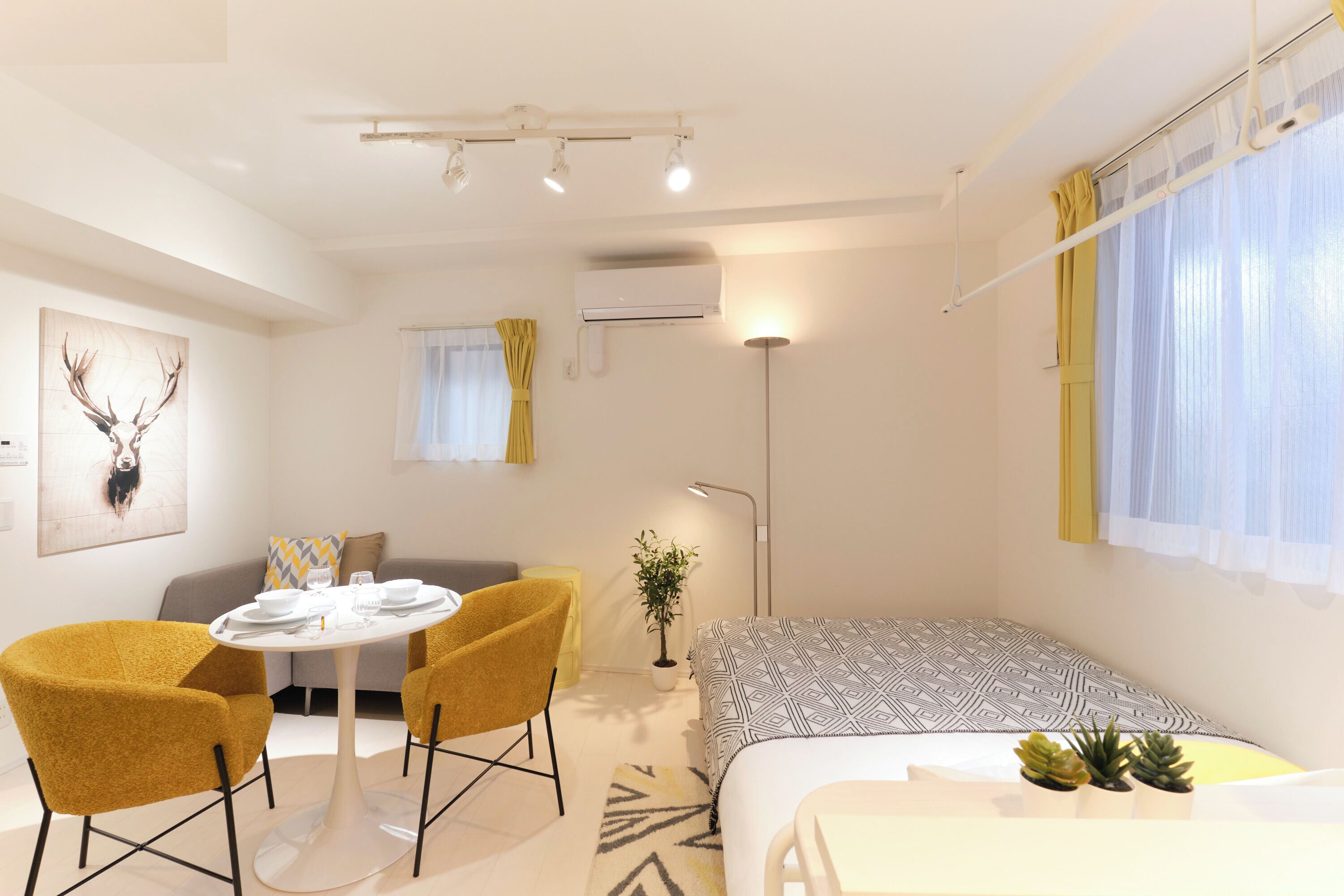 Une chambre d’hôtel moderne comprenant un lit, une table de salle à manger ronde avec des chaises, un canapé, une plante en pot et un climatiseur fixé au mur.