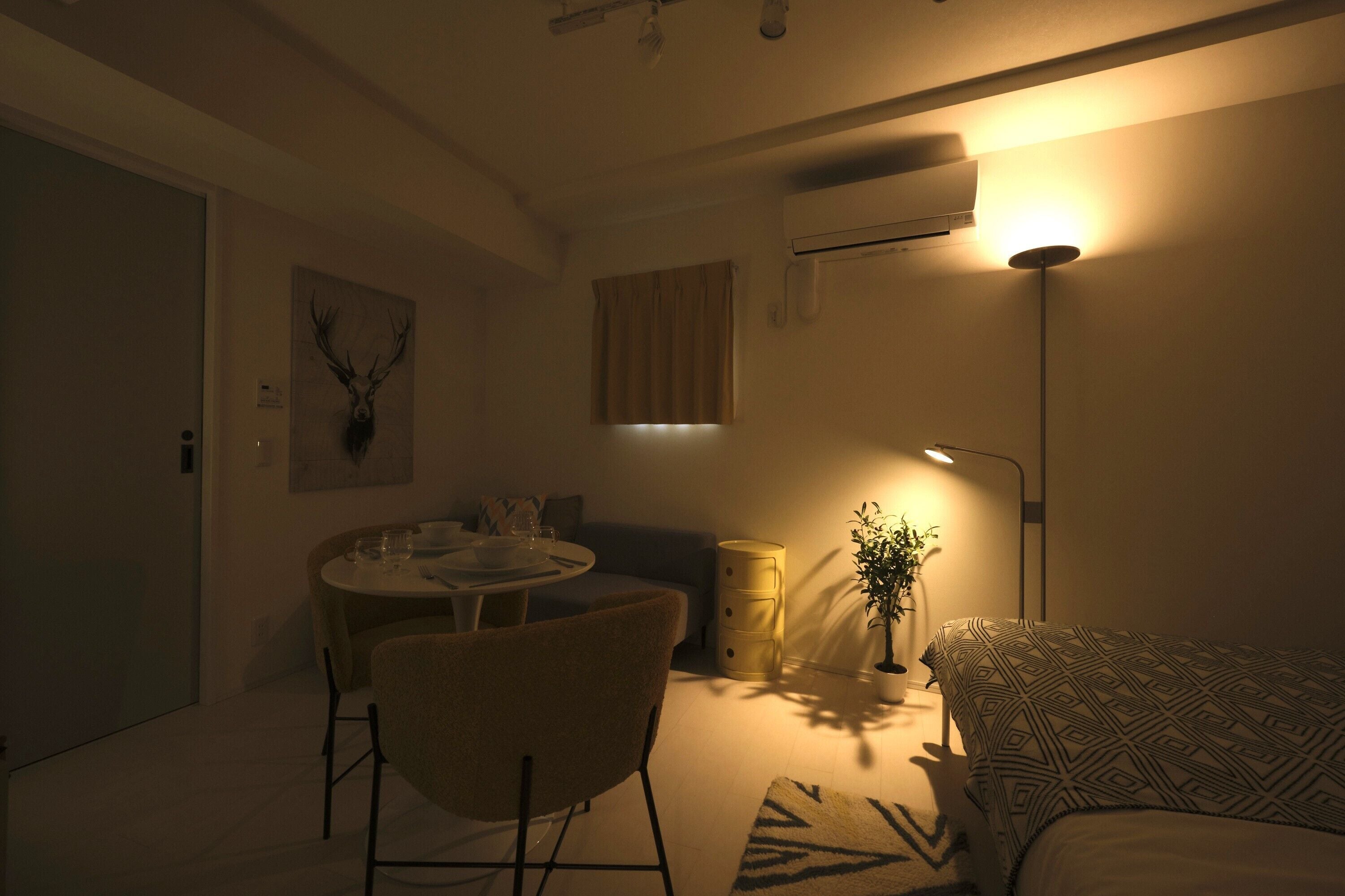 A dimly lit room with a dining table, a sofa, a lamp, and a wall-mounted air conditioner.