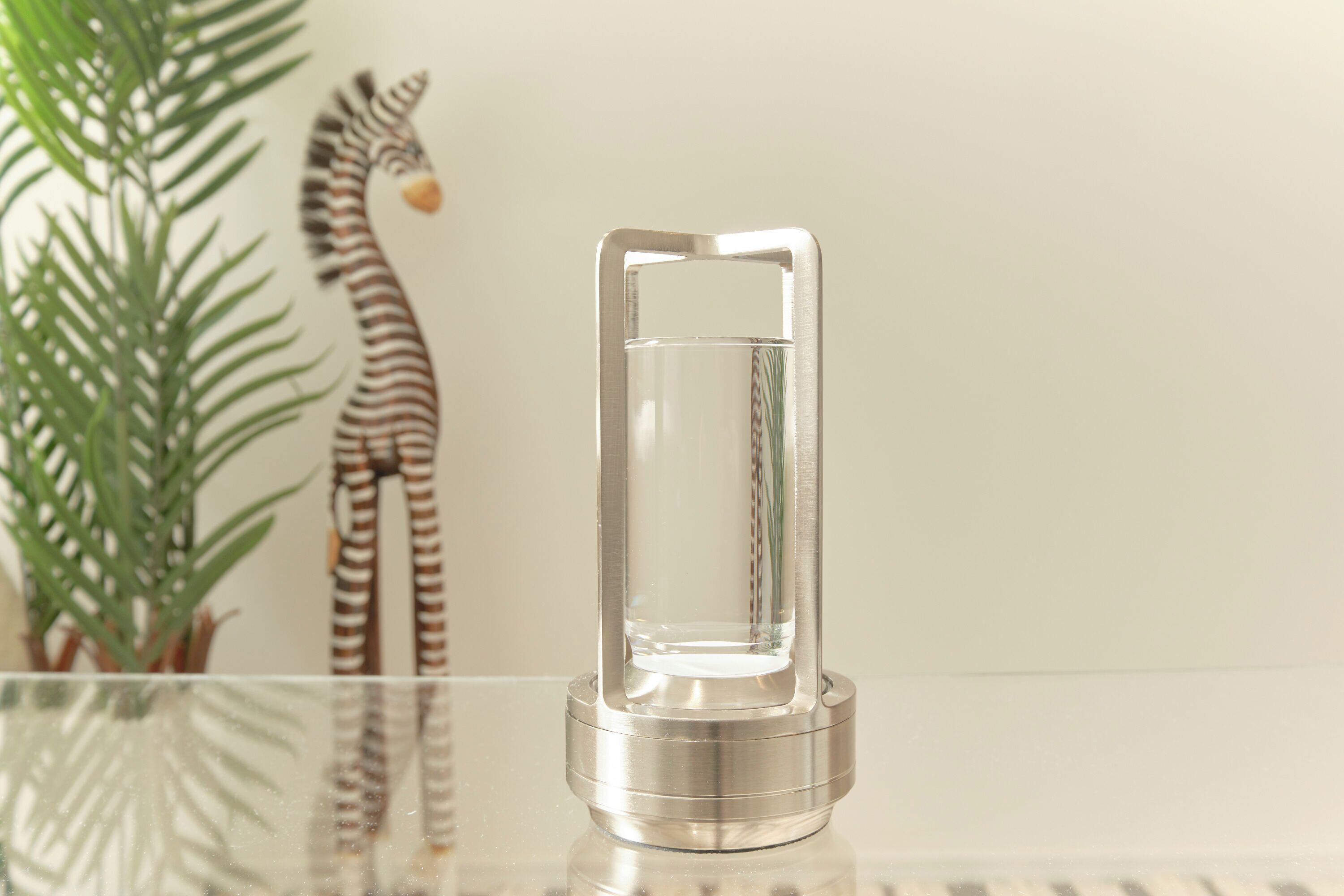 A clear glass bottle with a metallic base on a reflective surface.