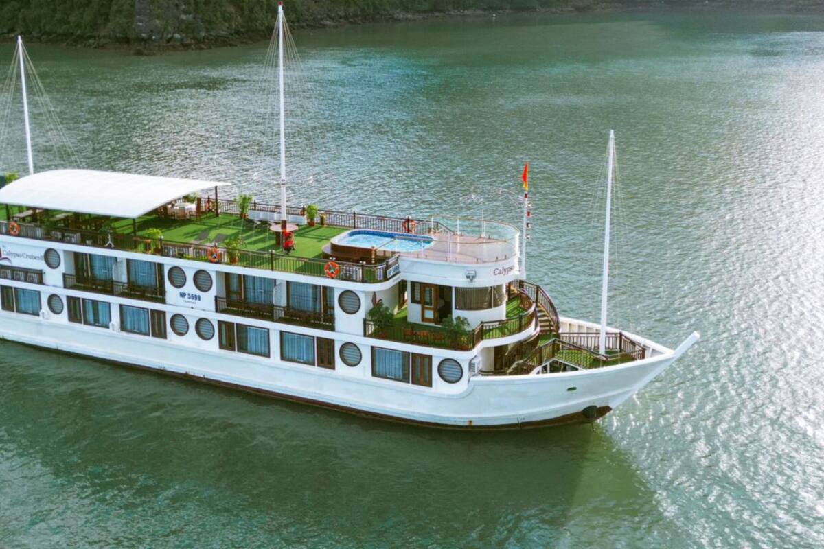 A large, multi-deck river cruise ship with outdoor deck areas, multiple windows, and a flag at the stern.