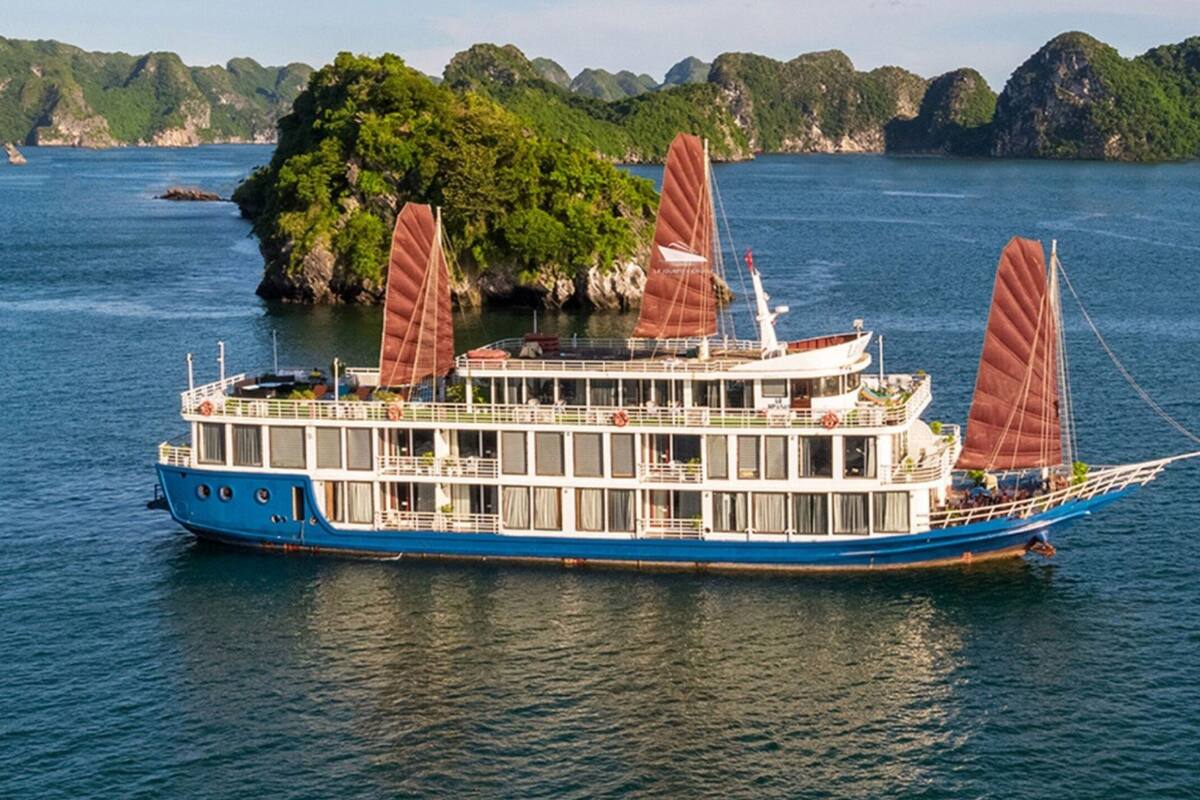 A large blue and white riverboat with multiple decks and a cabin structure, floating on calm water with a backdrop of green hills.