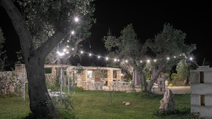 Un espace extérieur comprenant un bâtiment en pierre, un grand arbre et des guirlandes lumineuses.