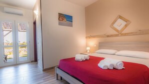 Une chambre d’hôtel avec un lit, une couverture rouge, une table de chevet avec une lampe et un tableau au mur.