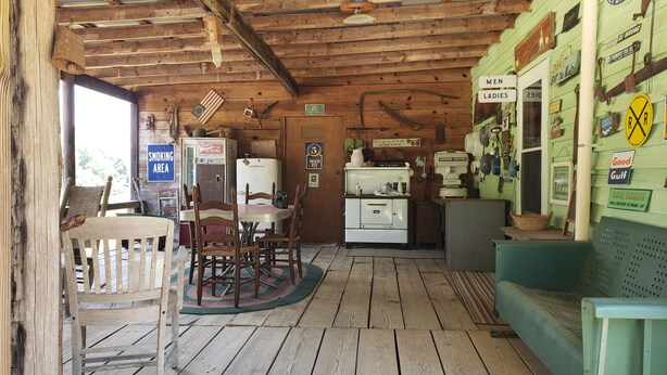 Interior rústico de una cabaña con pisos de madera, una mesa de comedor con sillas, un refrigerador, un lavamanos y varios carteles en las paredes.
