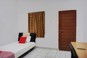 A small, clean room with a bed, a wooden door, and a small table. - Super OYO Resident- K Syariah (Medan)