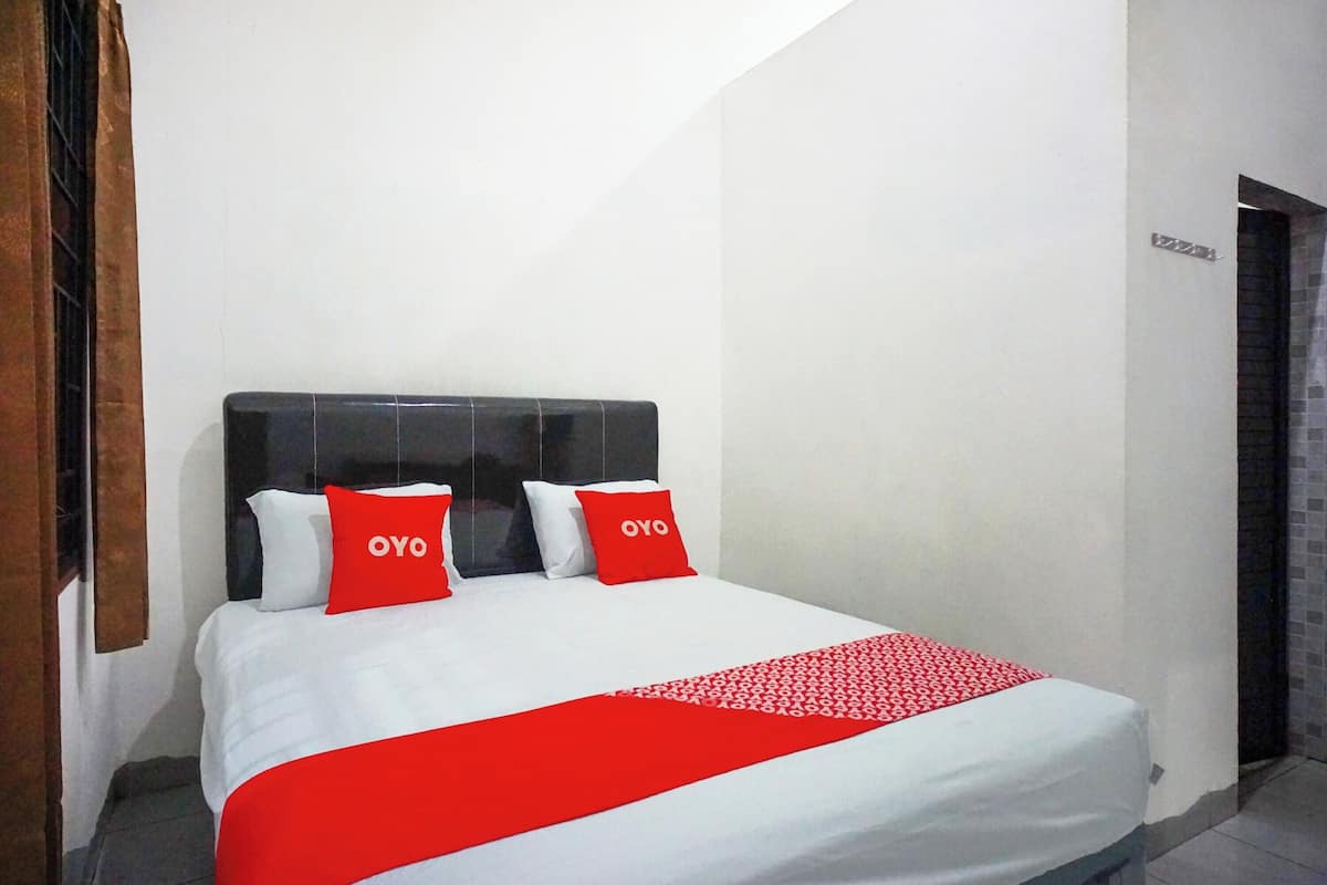 Hotellihuone, jossa on sänky, kaksi punaista koristetyynyä, joissa on OYO-logo, valkoinen päiväpeite ja punainen pöytäliina.