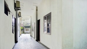 A narrow hallway with tiled flooring, white walls, and several doors and windows. - Super OYO Resident- K Syariah (Medan)