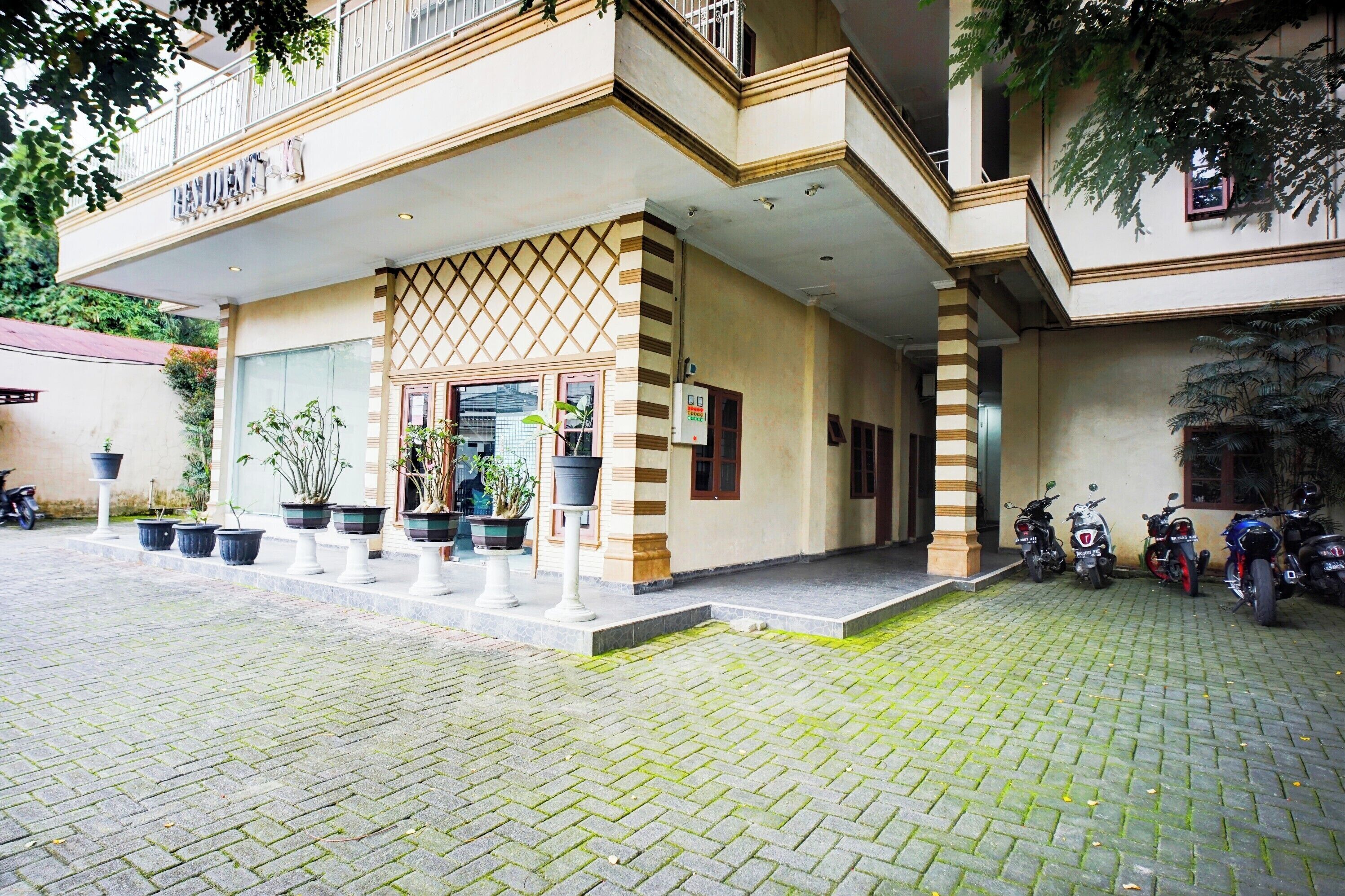 A hotel entrance with a covered walkway, potted plants, and motorcycles parked outside.