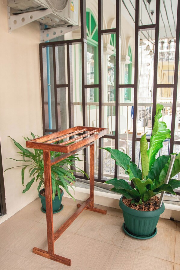 Un banco de madera en una habitación con ventanas amplias, plantas en macetas y suelo de baldosas.