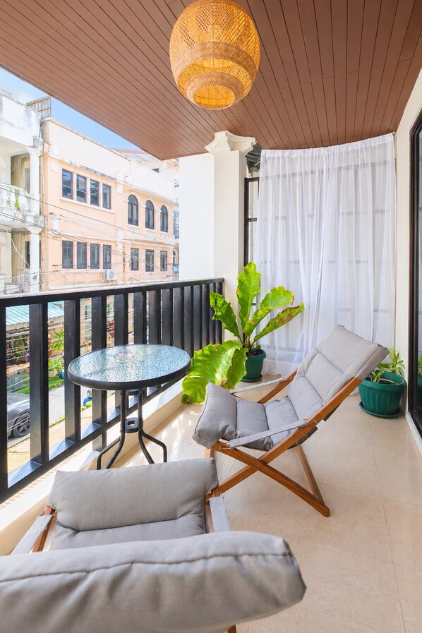 A balcony with a round table, two cushioned chairs, a potted plant, and a hanging light fixture.